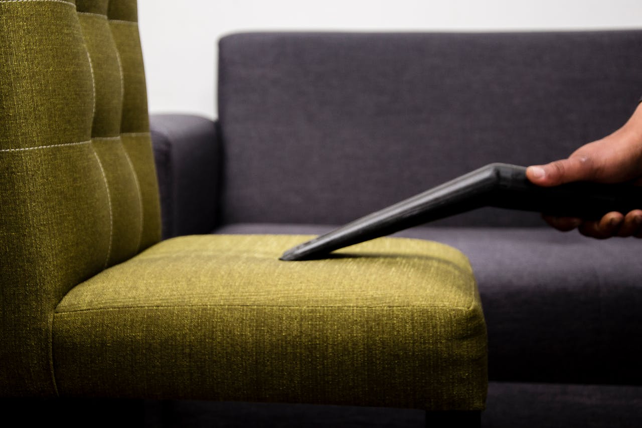 Close-up of a person vacuuming a modern sofa chair indoors, highlighting cleaning service.